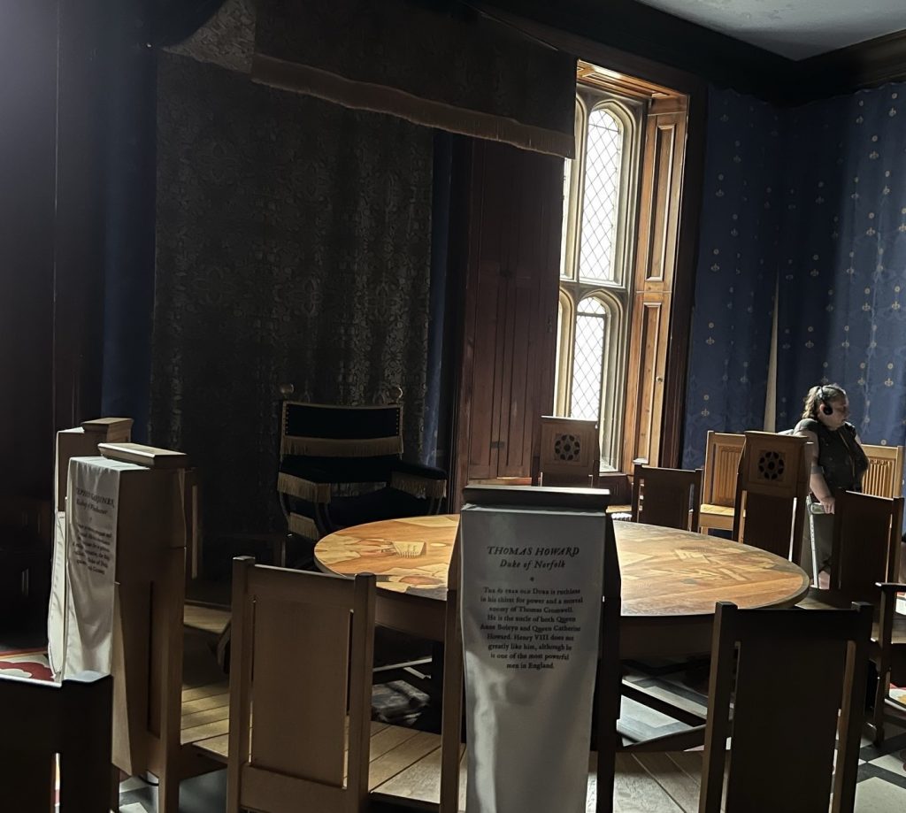 Kings Council room. Round table with chairs and dark paneling. Fireplace and windows on the exterior wall.