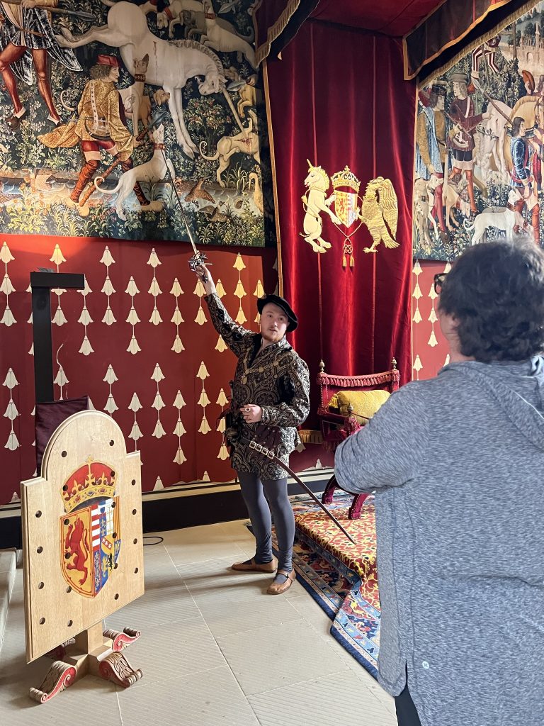 Continuing around the room the character actor is explaining the meaning of the tapestries and using his sword is pointing out the various images within the tapestries. In this instance the horn of the Unicorn is touching a wounded dog to heal the dog. This corelates to the healing that Christ brings.