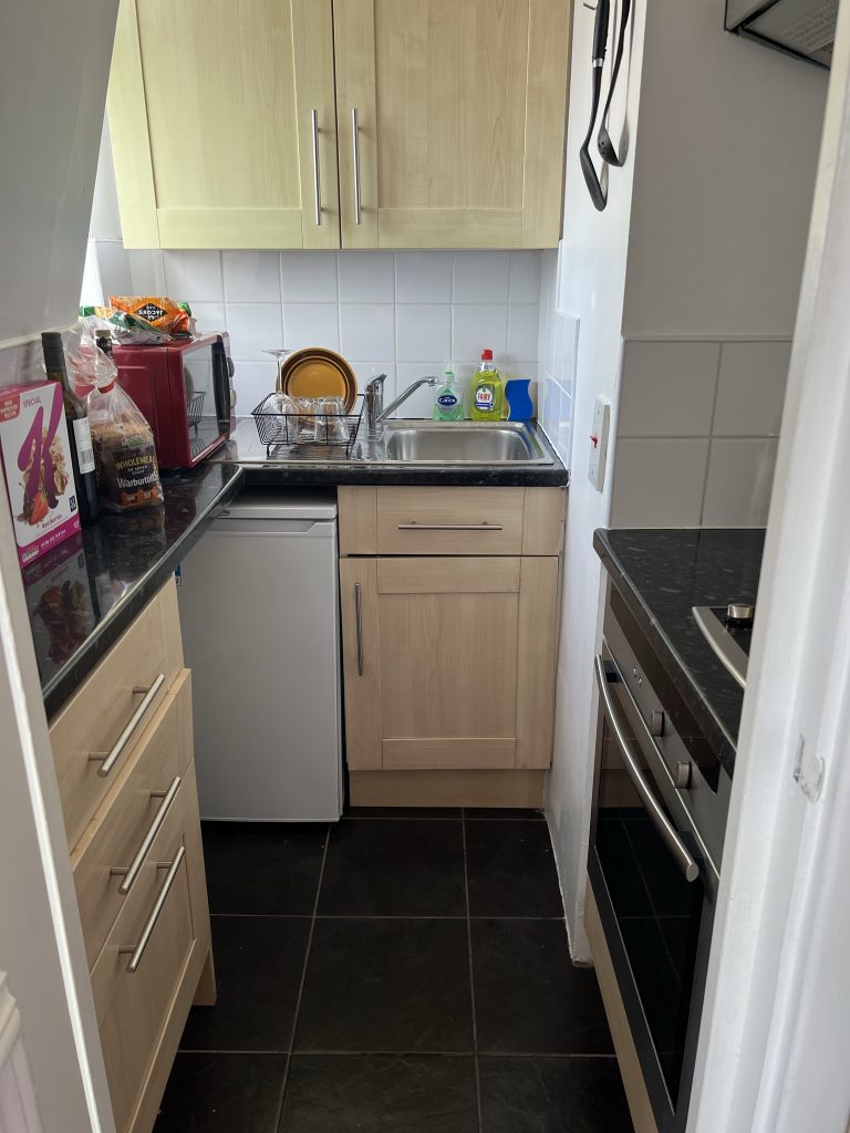 Small kitchen only 5 foot by 5 foot. At the end is a sink and small refrigerator with two cabinets. Along the two sides are three drawers with a countertop on one side and a small stove on the other.
