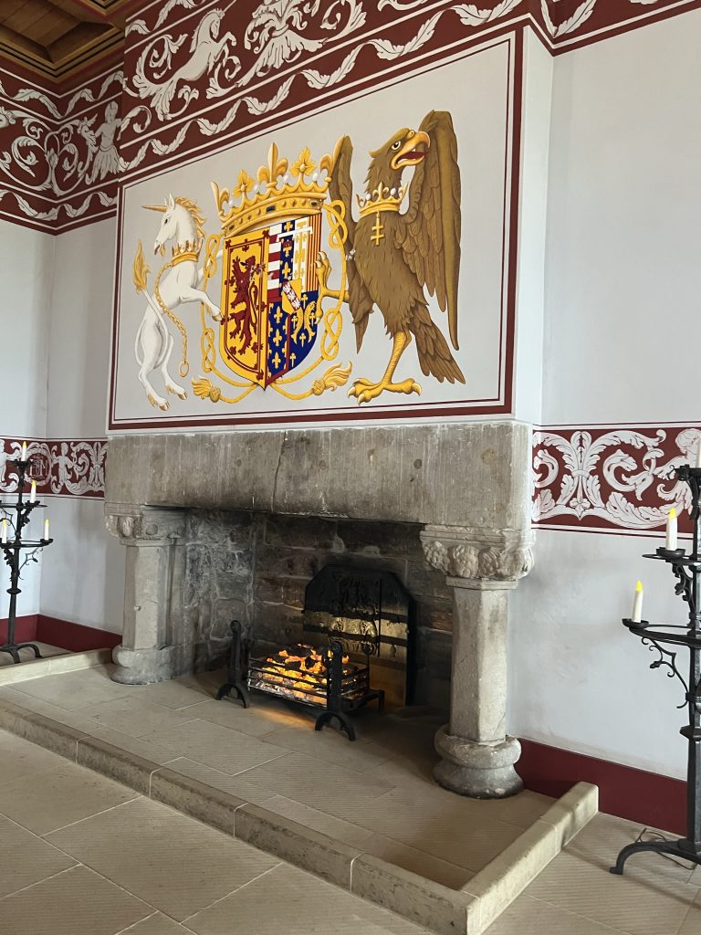 A large fireplace with a brightly painted picture of the Unicorn, the shield of the Stewarts and the Eagle. The walls are painted white with a decorative dark red border half way up the wall and a wider ceiling border.