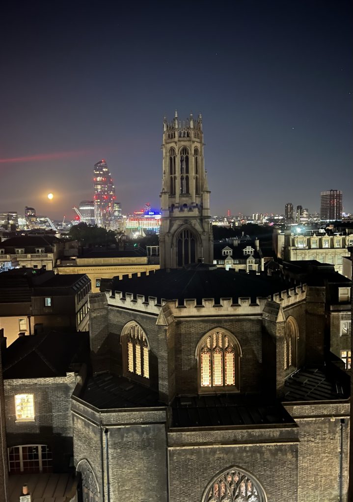 Image from the flat at night with the lights on in the church and the night lights of London and a full moon.
