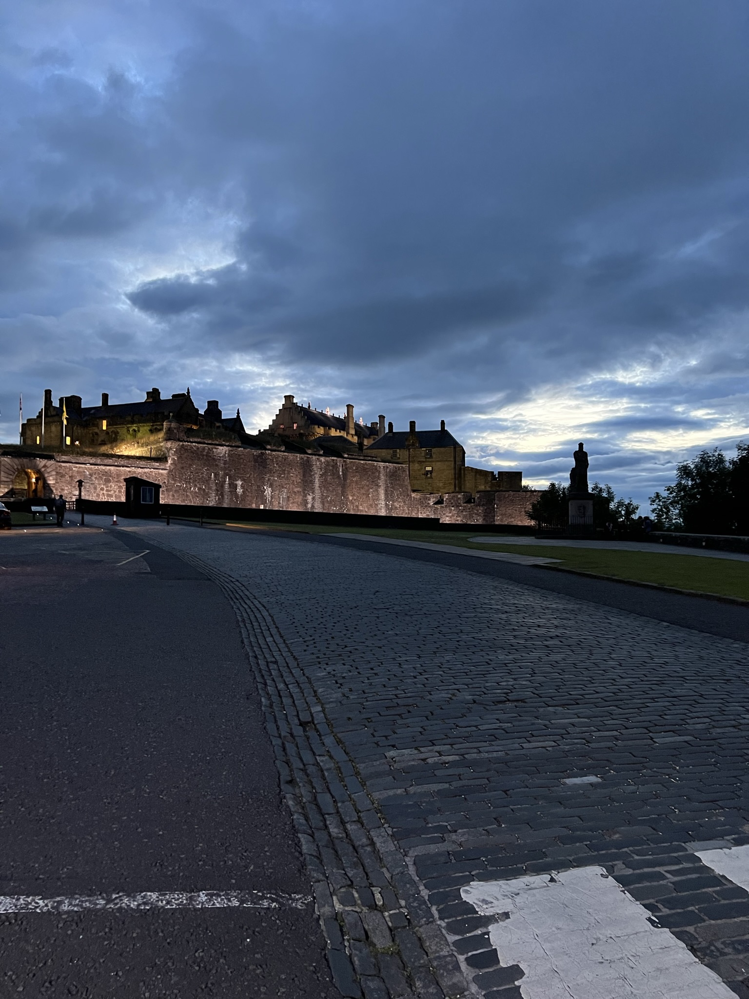 Image of the Castle at dusk. The castle outer walls are lit up against the dark cloudy Scottish night. 
