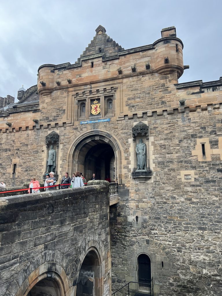Entrance to Stirling Castle.  The stone walkway leads up to the arched entrance of the castle.  On either side of the arch are two statutes - one of William Wallace and one of Robert the Bruce.  Beside each statute are the cut outs for the archers to shoot through.  Above the statutes is the emblem of Scotland - a red lion on a yellow shield background.  Decorative stone work add to the grand entrance. 
