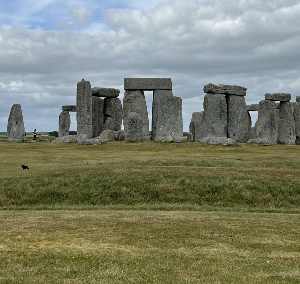 Image of Stonehenge from the distance. The original ditch is visible with three sets of upright stones and lentils.