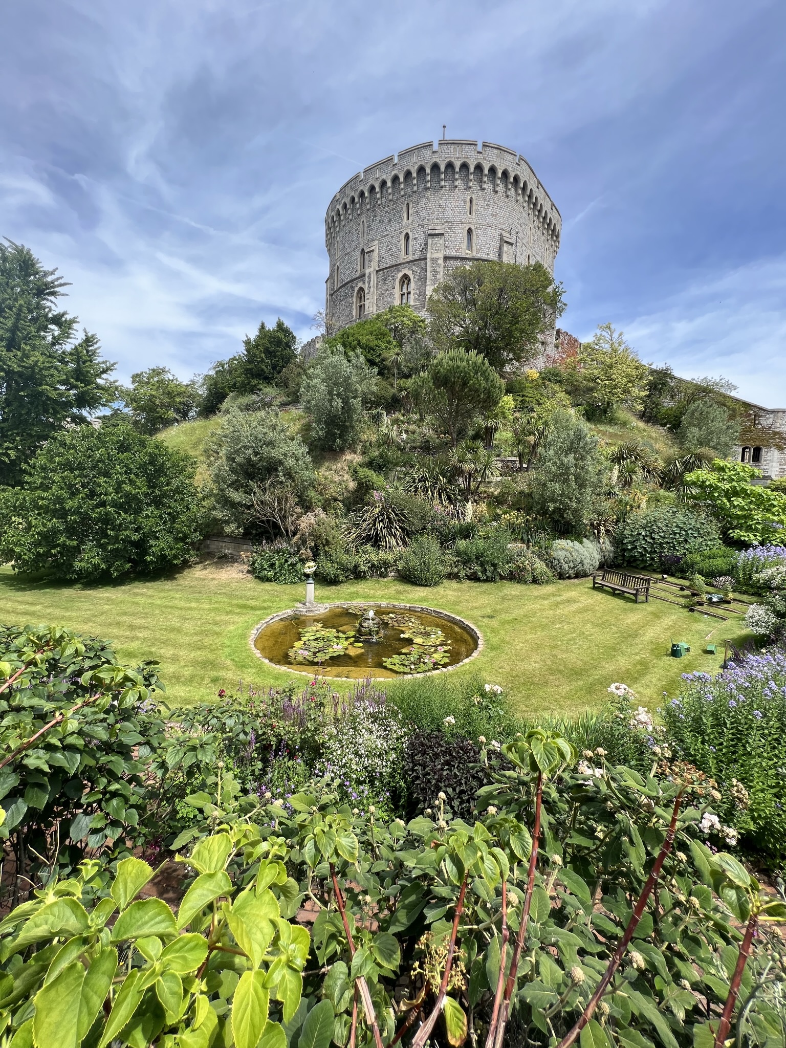 Image of the gardens below the round tower. Plants, flowers, and a small stream lead up the hill to the round tower.