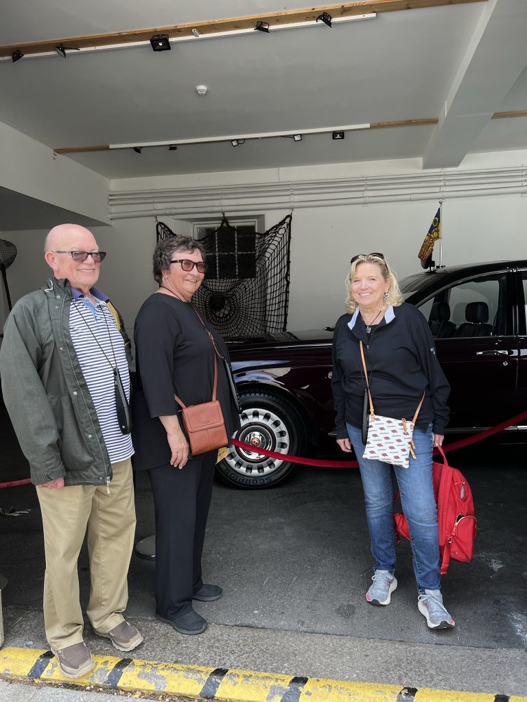 Scott, Kathy, and Kay standing in front of the dark red Bentley parked in the garage at Balmoral. 
