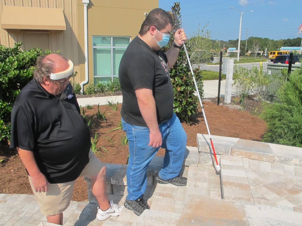 Kenny teaching a client how to navigate steps using a white cane.